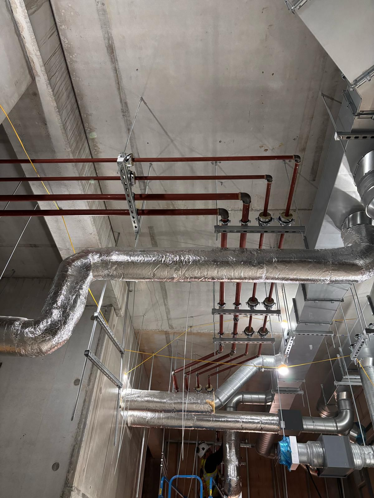 Insulated pipework and silver ducting running across a concrete plant room ceiling