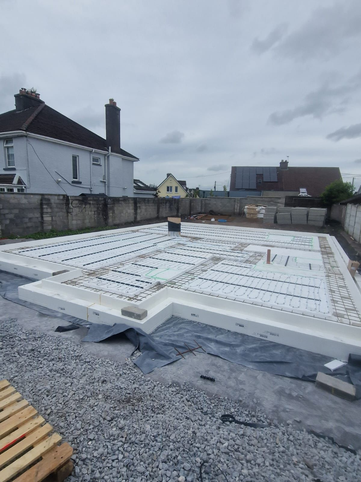 New-build foundation slab with underfloor insulation laid out, houses behind