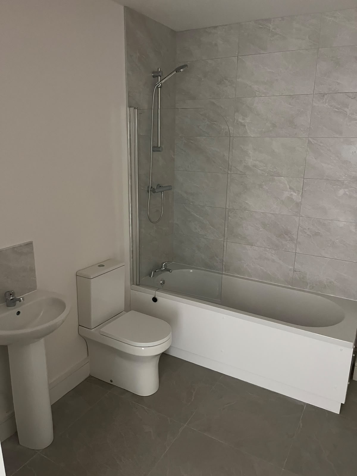 Finished bathroom with a white bath, close-coupled toilet and pedestal basin on grey tiles