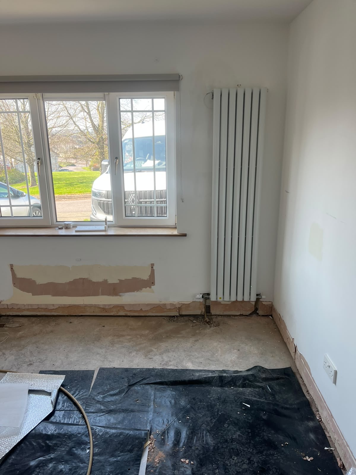Room mid-renovation with a new white vertical radiator fitted under the window