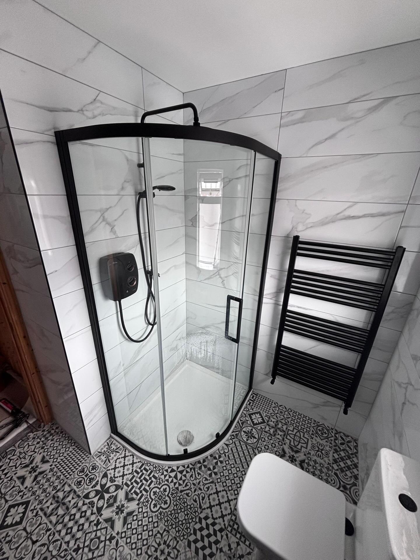 Black-framed quadrant shower beside a black towel rail, with patterned monochrome floor tiles
