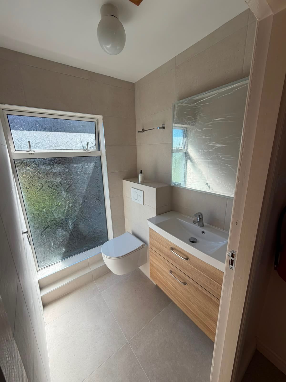 Finished en-suite with a wall-hung toilet, wood vanity unit and a large mirror